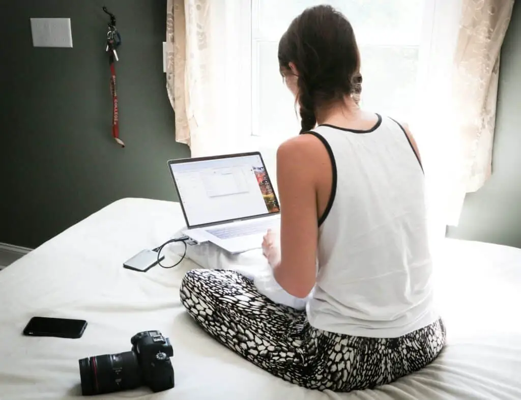 screen time, woman in white tank top sitting on bed in front of laptop computer