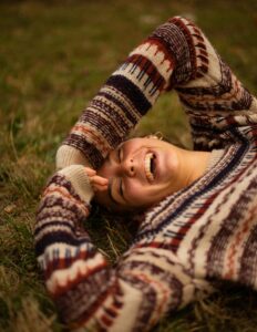 laughter, woman in brown and white sweater lying on green grass field during daytime