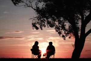 silhouette of two people sitting on chairs near a tree