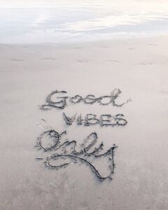 An image of a sandy beach with the words 'Good Vibes Only' written in the sand