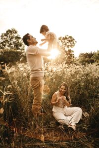 Man lifting girl in air next to a woman sitting on the floor smiling