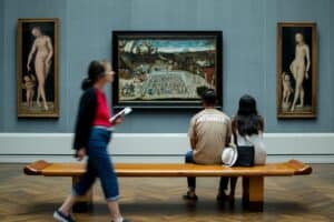man and woman sitting on bench while looking at painting